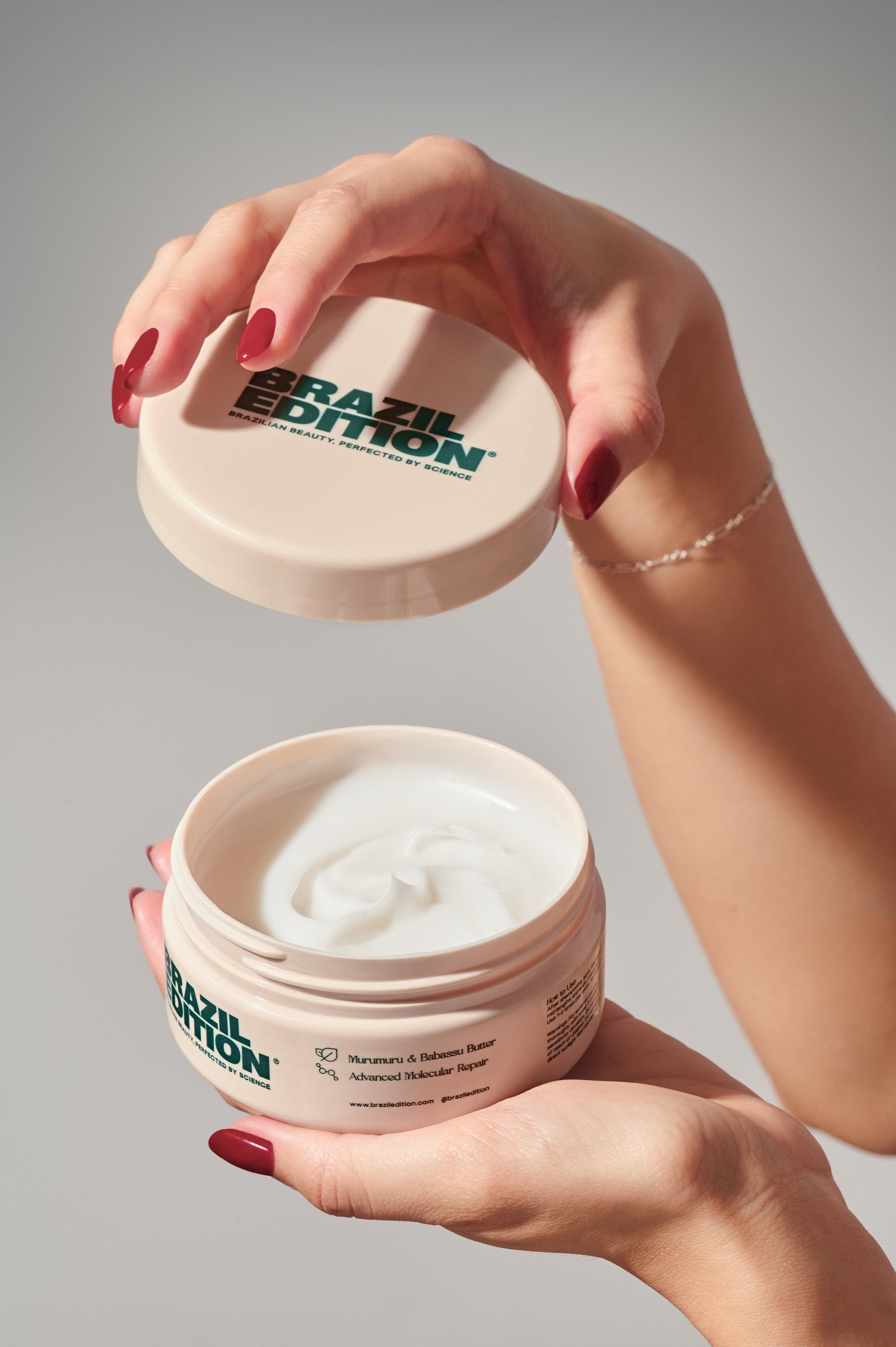 Person holding a 'Brazil Edition' skincare product jar with white cream inside on a gray background